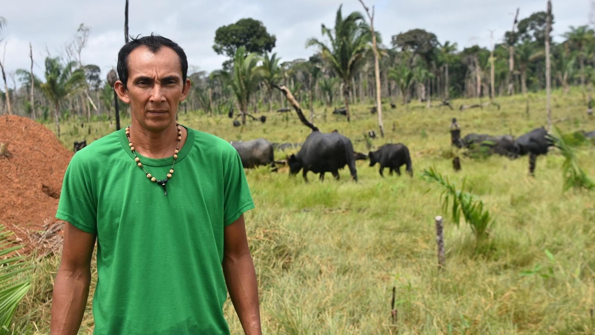 Junger Brasilianer steht mit mürrischem Gesicht vor einer Weide mit Büffeln