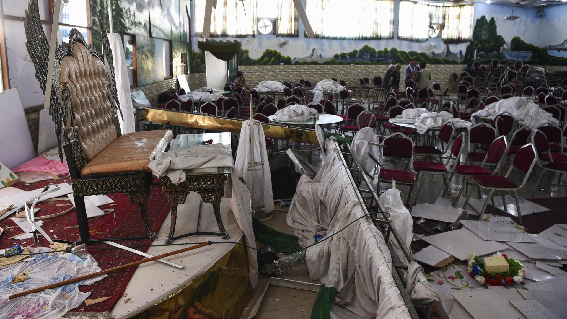 Im Vordergrund des Bildes ist ein durch eine Explosion zerstörter Hochzeitssaal in Kabul zu sehen, im Hintergrund untersuchen Männer den Raum. Im Vordergrund des Bildes ist ein durch eine Explosion zerstörter Hochzeitssaal in Kabul zu sehen, im Hintergrund untersuchen Männer den Raum.