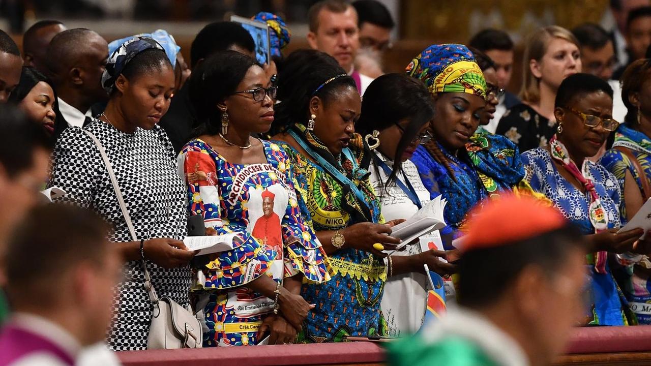 Frauen aus der Amazonas-Region stehen während der Messe in den Kirchenbänken. Daneben: Geistliche und Messdiener. Frauen aus der Amazonas-Region stehen während der Messe in den Kirchenbänken. Daneben: Geistliche und Messdiener.