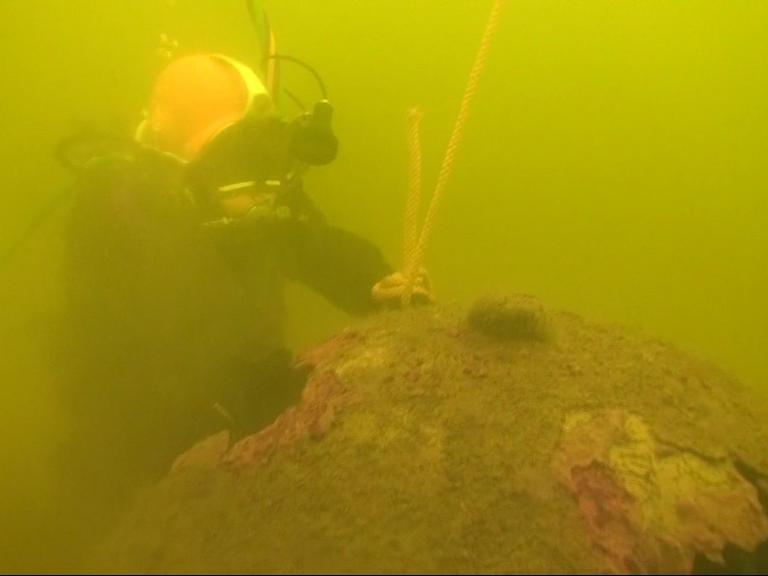 Im trüben Wasser befestigt ein Taucher ein Seil an einer alten, verrosteten Ankertaumine. Im trüben Wasser befestigt ein Taucher ein Seil an einer alten, verrosteten Ankertaumine.
