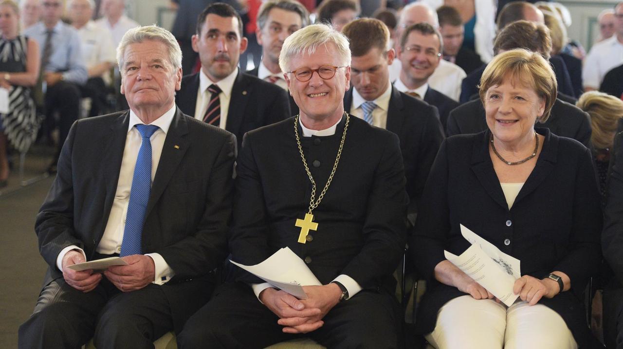 Bundeskanzlerin Angela Merkel (CDU, r-l), der Vorsitzende des Rates der EKD, Landesbischof Heinrich Bedford-Strohm und Bundespräsident Joachim Gauck sitzen am 02.07.2015 in Berlin beim Johannisempfang der Evangelischen Kirche in Deutschland (EKD) in der Französischen Friedrichstadtkirche am Gendarmenmarkt in Berlin auf ihren Plätzen. Foto: Rainer Jensen/dpa | Bundeskanzlerin Angela Merkel (CDU, r-l), der Vorsitzende des Rates der EKD, Landesbischof Heinrich Bedford-Strohm und Bundespräsident Joachim Gauck sitzen am 02.07.2015 in Berlin beim Johannisempfang der Evangelischen Kirche in Deutschland (EKD) in der Französischen Friedrichstadtkirche am Gendarmenmarkt in Berlin auf ihren Plätzen. Foto: Rainer Jensen/dpa |