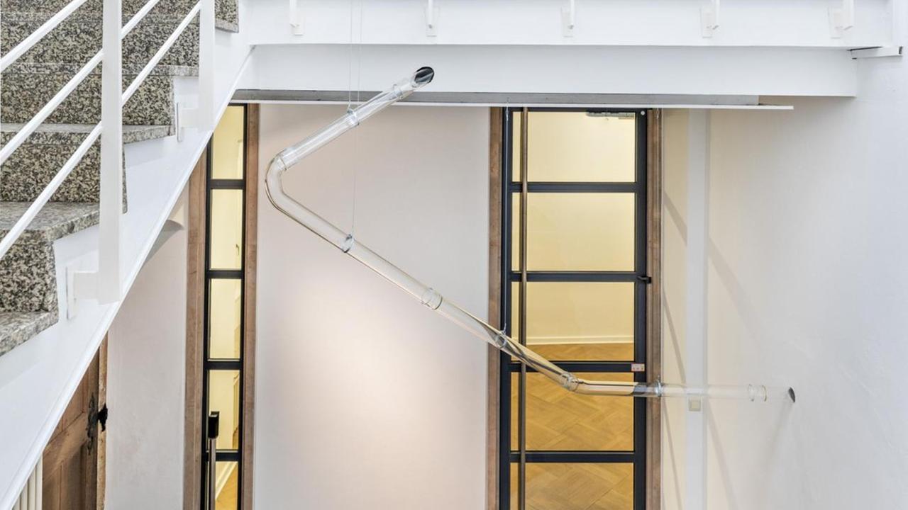 Eine gläserne Leitung, die an eine Rohrpost erinnert, läuft durch nahezu alle Räume der Ausstellung. Dafür wurden Wände und Decken durchbrochen. Zu sehen sind darin Haare, Staub und weißes Granulat, spärlich verteilt. Eine gläserne Leitung, die an eine Rohrpost erinnert, läuft durch nahezu alle Räume der Ausstellung. Dafür wurden Wände und Decken durchbrochen. Zu sehen sind darin Haare, Staub und weißes Granulat, spärlich verteilt.