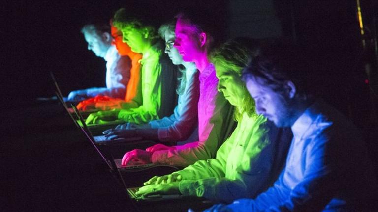 Bunt angestrahlte Musiker sitzen konzentriert vor Laptops. Bunt angestrahlte Musiker sitzen konzentriert vor Laptops.