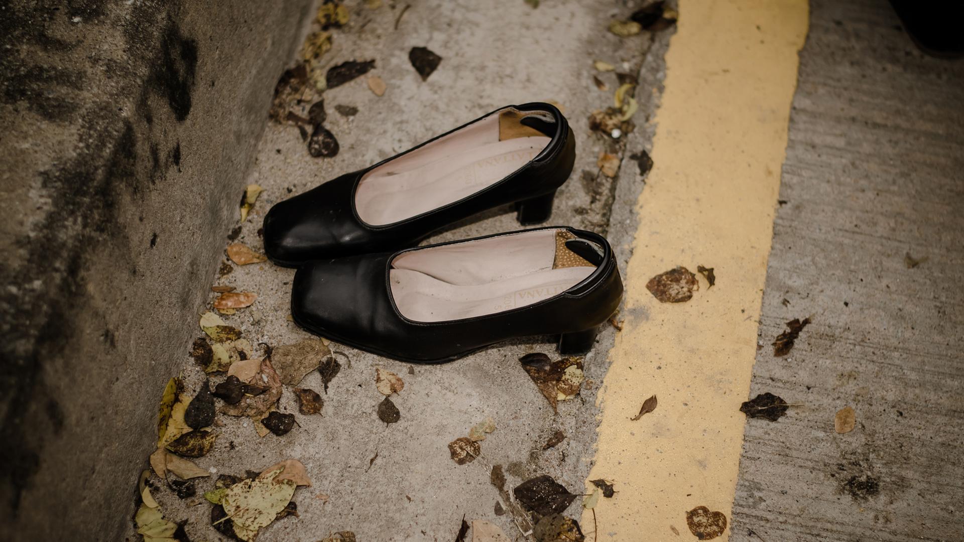 Ein paar schwarze ausgetretene Damenschuhe stehen auf einer Straße mit Laubblättern Ein paar schwarze ausgetretene Damenschuhe stehen auf einer Straße mit Laubblättern