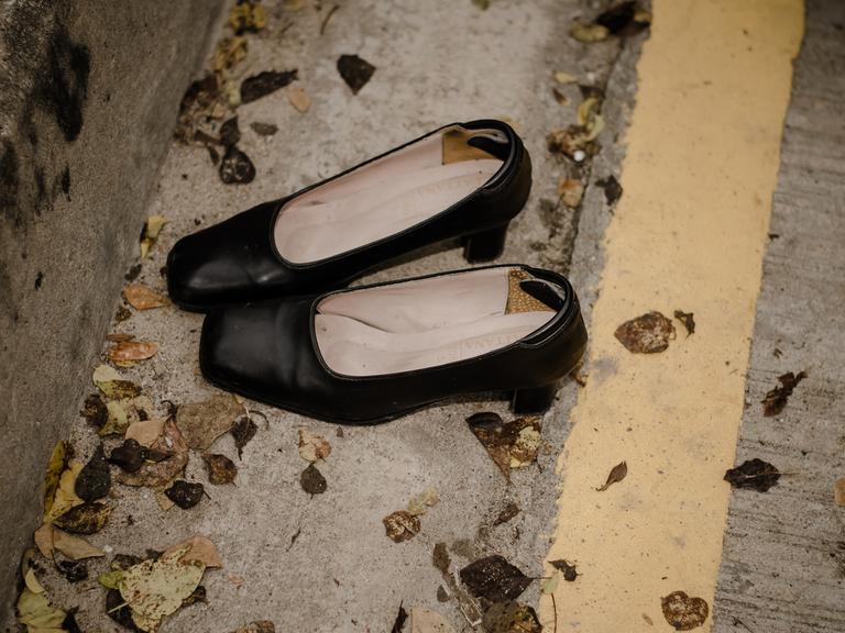 Ein paar schwarze ausgetretene Damenschuhe stehen auf einer Straße mit Laubblättern