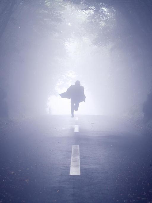 Ein schemenhafter Mann flüchtet auf einer Straße, die durch einen Wald führt