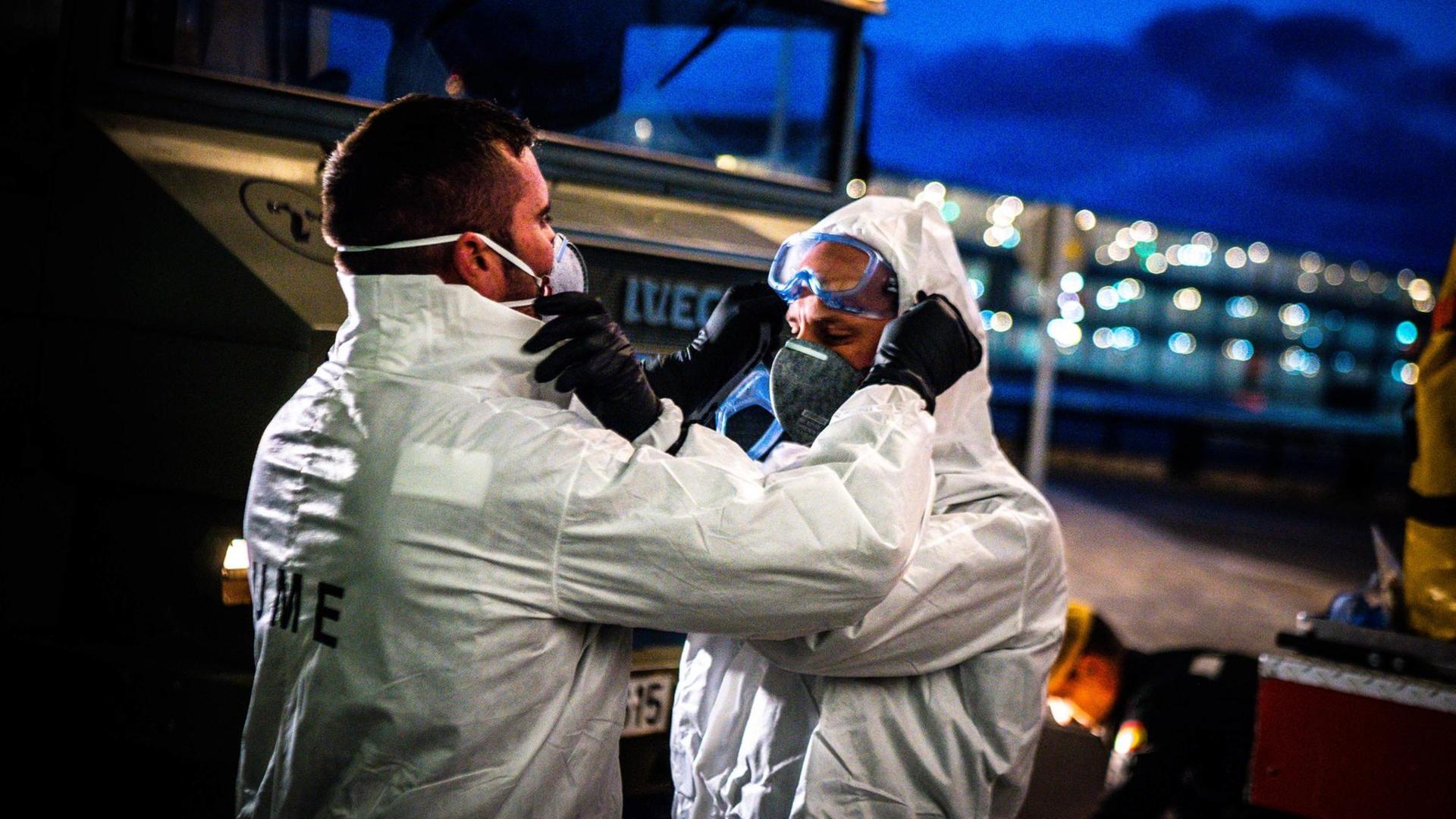 Das Foto zeigt zwei Helfer in Schutzanzügen im Einsatz gegen das Coronavirus. Das Foto zeigt zwei Helfer in Schutzanzügen im Einsatz gegen das Coronavirus.