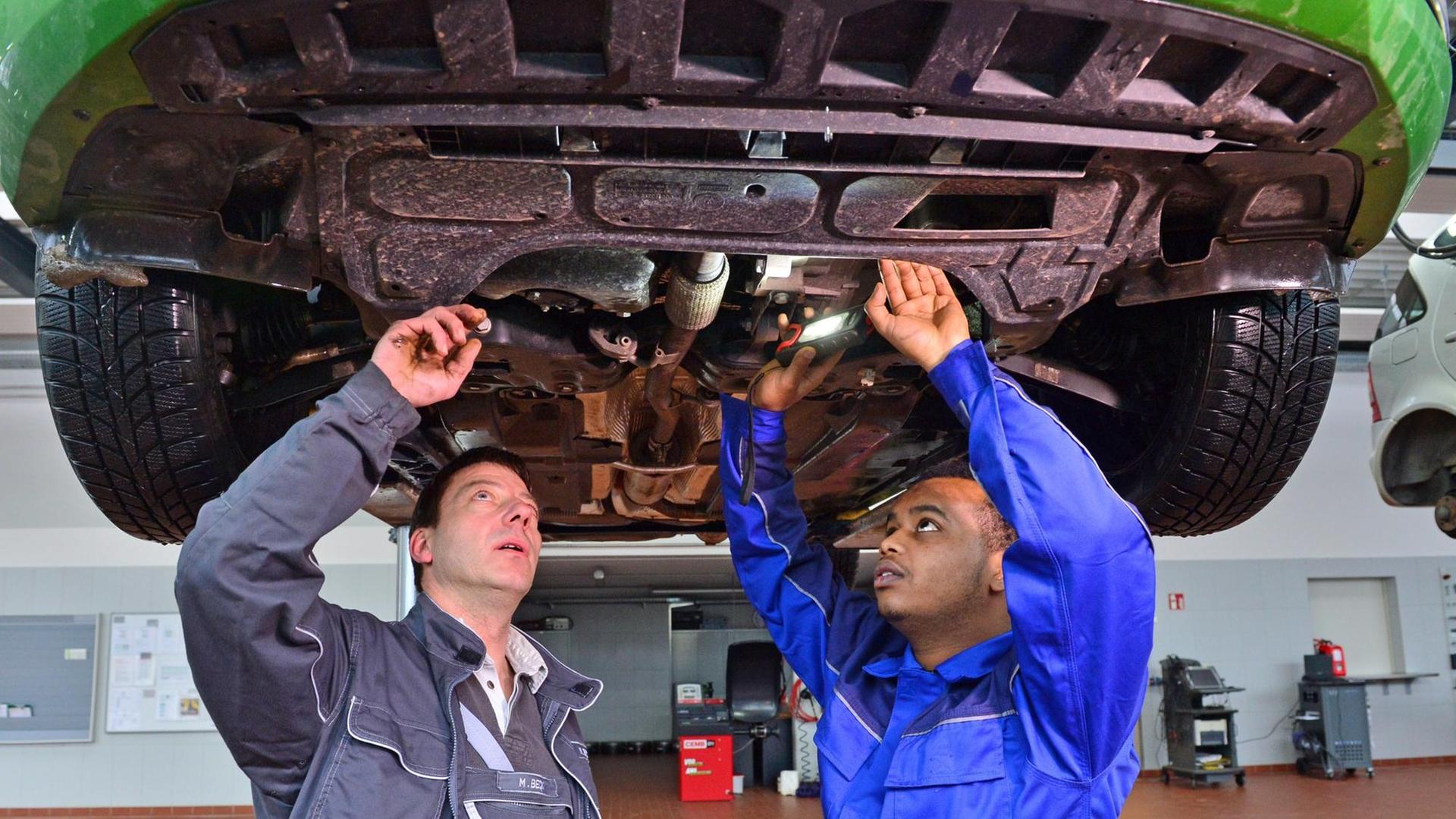 Ein Flüchtling und ein Servicetechniker schauen sich ein Auto von unten an. Ein Flüchtling und ein Servicetechniker schauen sich ein Auto von unten an.