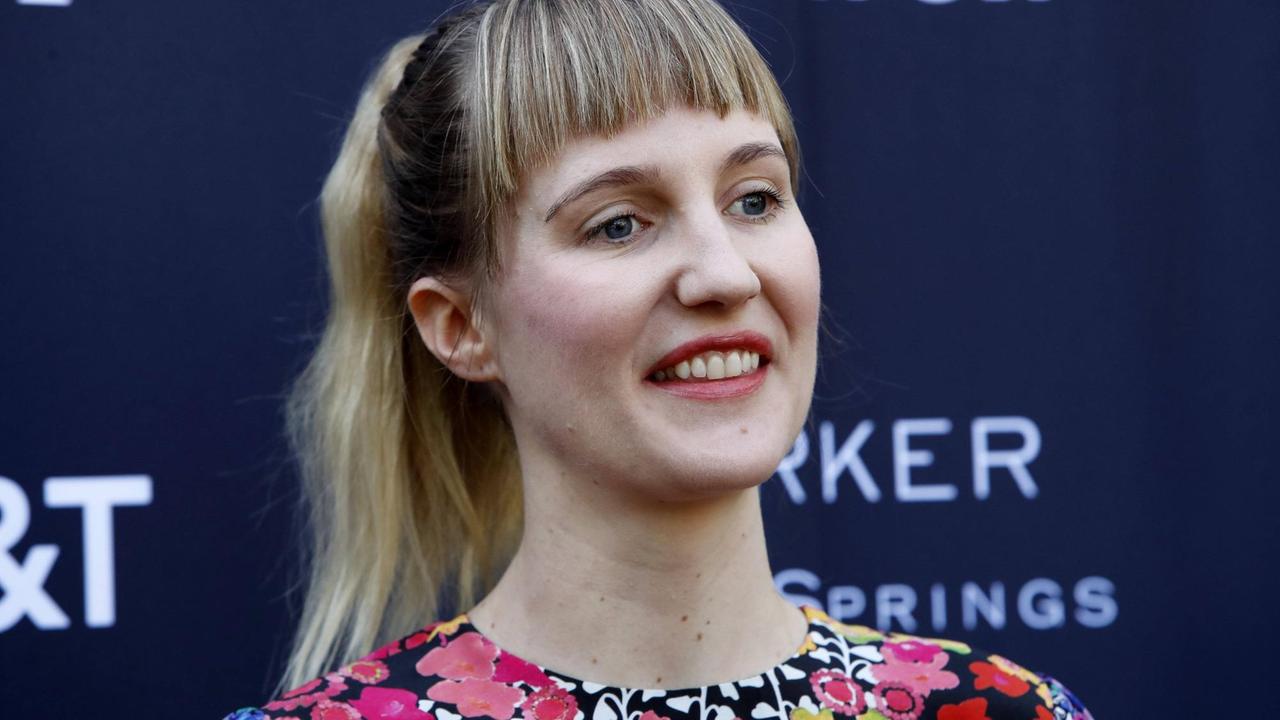 Eine junge Frau mit langen blonden Haaren und einen buntem Kleid lächelt in eine Kamera. Eine junge Frau mit langen blonden Haaren und einen buntem Kleid lächelt in eine Kamera.