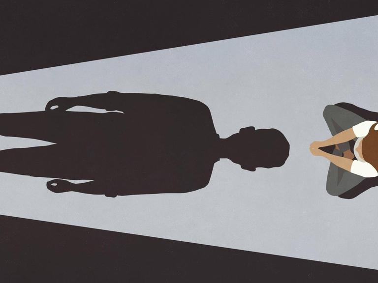 Eine Frau sitzt vor dem langen Schatten eines Mannes