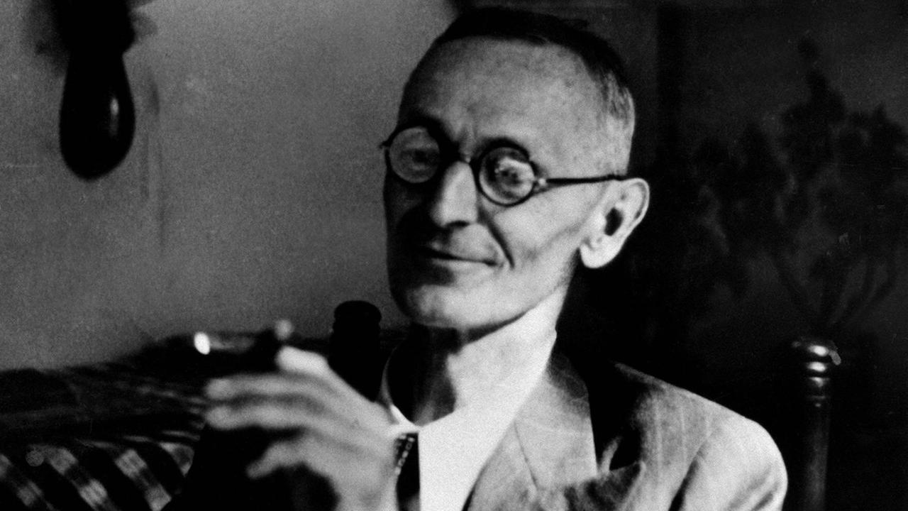 Der Schriftsteller Hermann Hesse sitzt in einem Zimmer und raucht Zigarre.