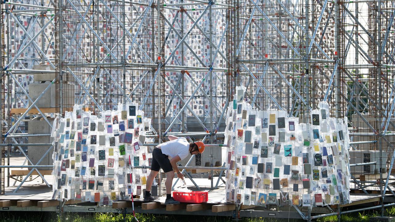 Ein Arbeiter hängt in Plastik eingehüllte Bücher an das Stahlgerüst des documenta-Kunstwerks "The Parthenon of Books" in Kassel. Ein Arbeiter hängt in Plastik eingehüllte Bücher an das Stahlgerüst des documenta-Kunstwerks "The Parthenon of Books" in Kassel.
