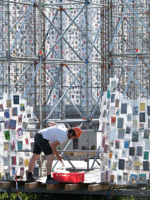 Ein Arbeiter hängt in Plastik eingehüllte Bücher an das Stahlgerüst des documenta-Kunstwerks "The Parthenon of Books" in Kassel.