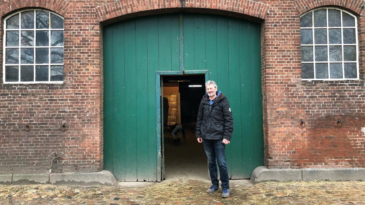 Der Landwirt Henning Kleinwort steht vor einem Backsteingebäude mit einem grünen Scheunentor. Der Landwirt Henning Kleinwort steht vor einem Backsteingebäude mit einem grünen Scheunentor.