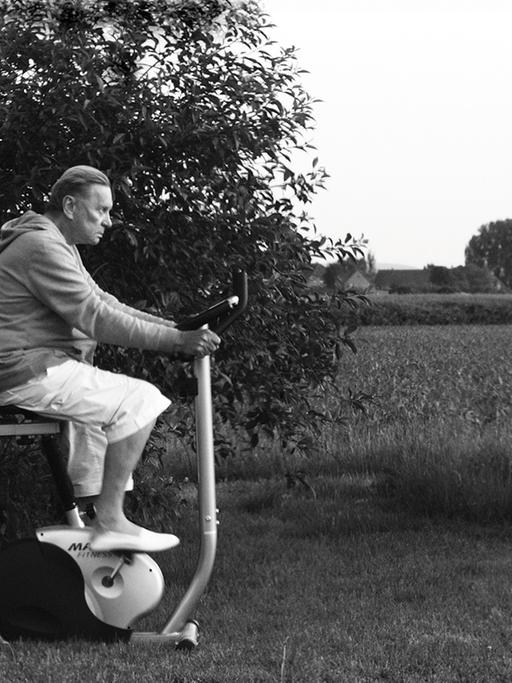 Helmut Berger auf einem Trimm-Dich-Fahrrad im Garten.