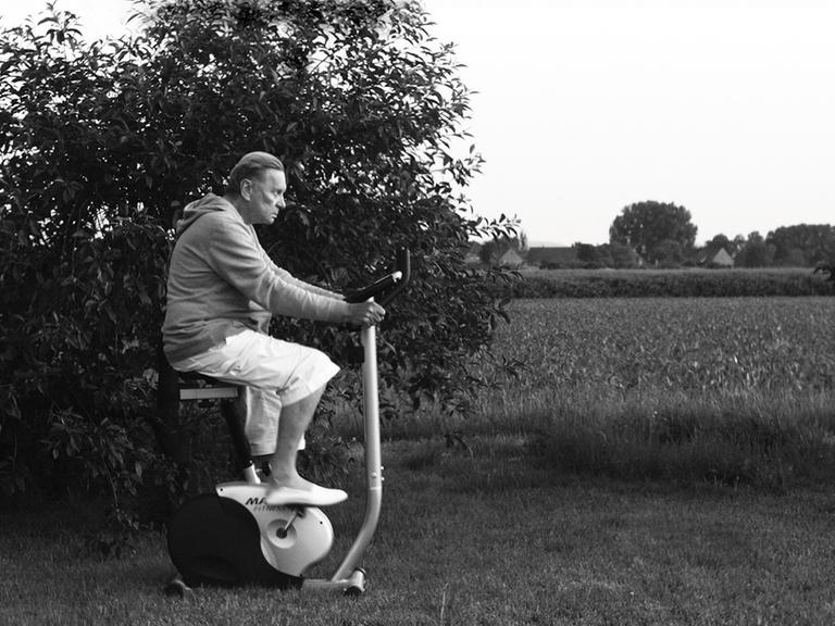 Helmut Berger auf einem Trimm-Dich-Fahrrad im Garten.