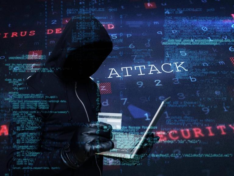 Symbolbild, das einen Hacker im Kapuzenpullover und mit Lederhandschuhen zeigt. In der Hand hält er eine Kreditkarte und ein Laptop.