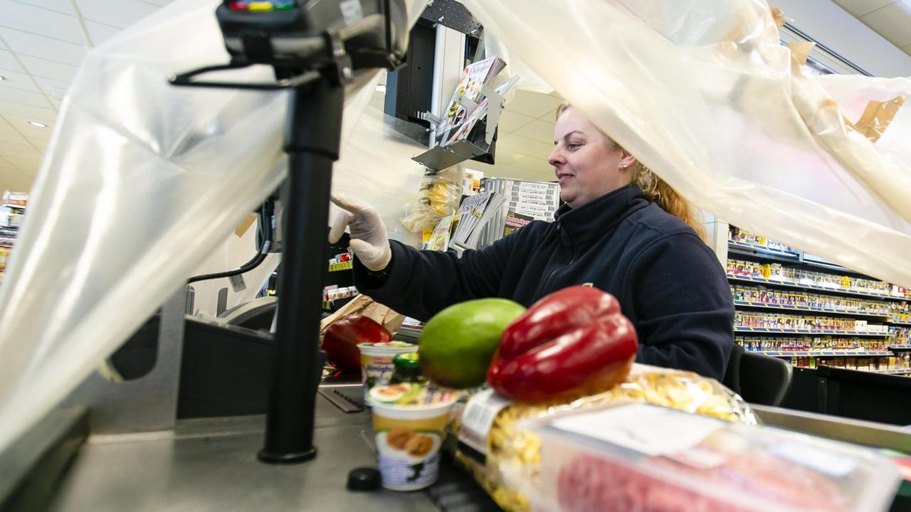 Ein Kassiererin arbeitet unter einer Plastikfolie, um sich vor Coronaviren zu schützen.