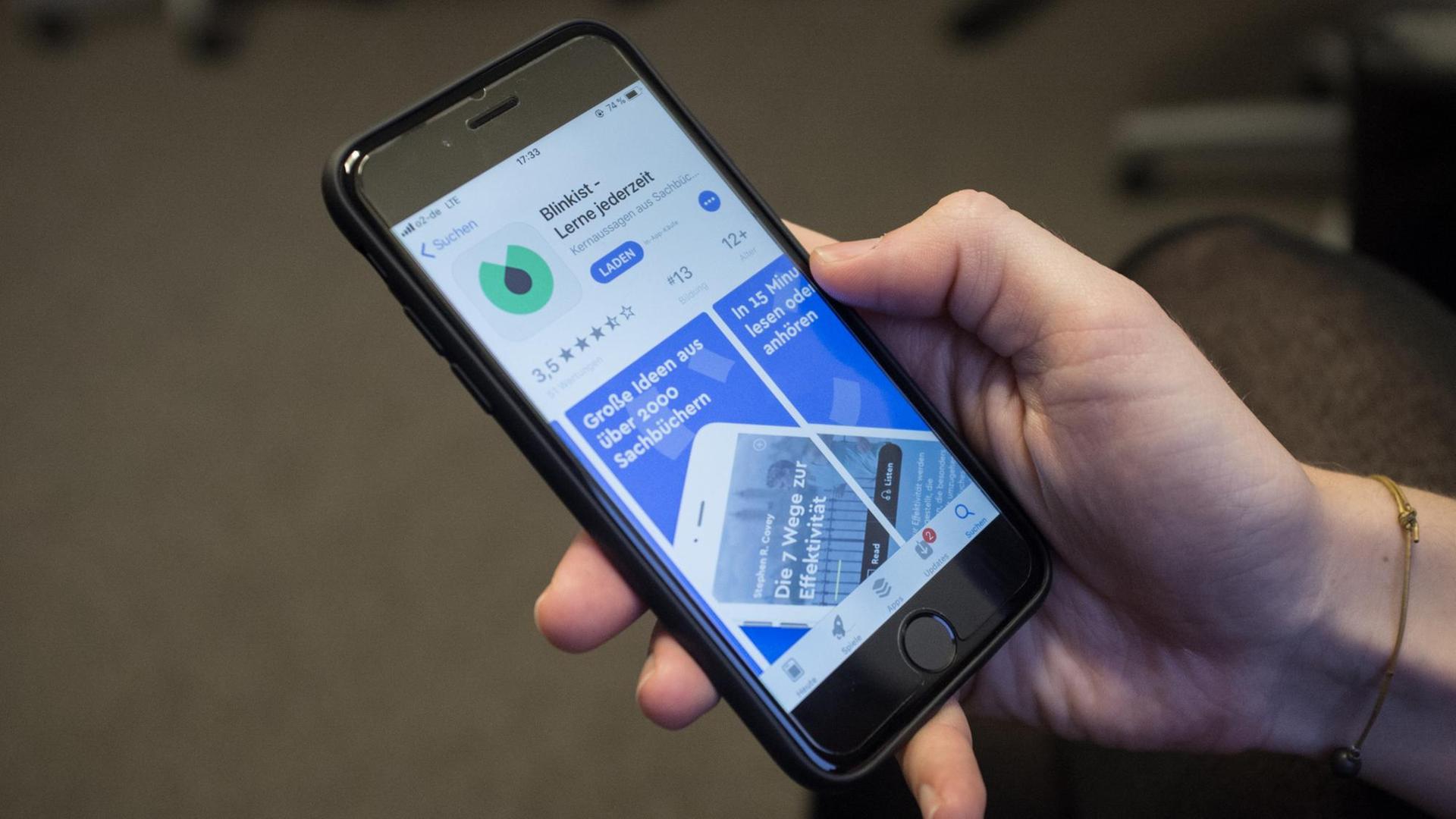 Eine Hand hält ein Smartphone. Auf dem Display ist die App Blinkist im App Store zu sehen.