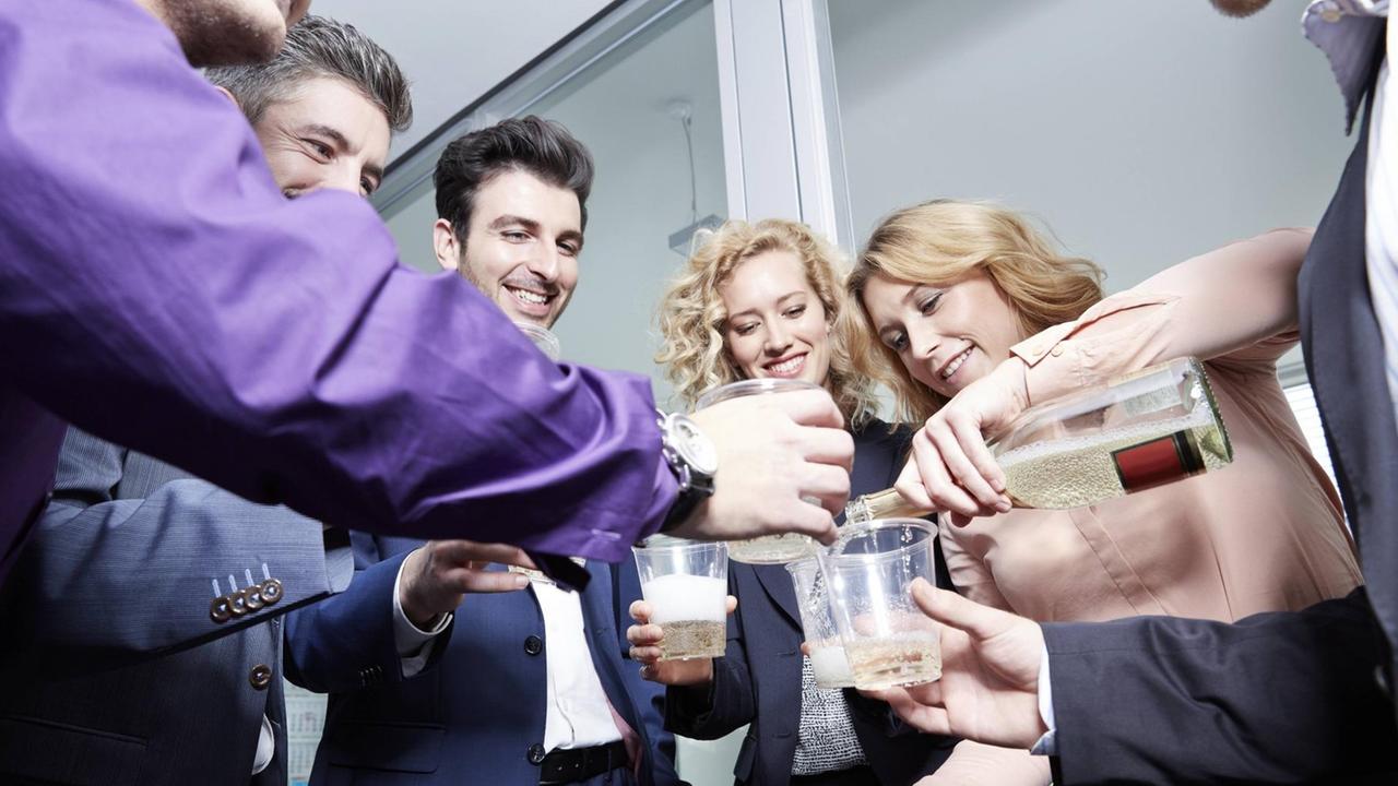 Menschen feiern in Büro, indem sie mit Sekt aus Plastikbechern anstoßen. Menschen feiern in Büro, indem sie mit Sekt aus Plastikbechern anstoßen.