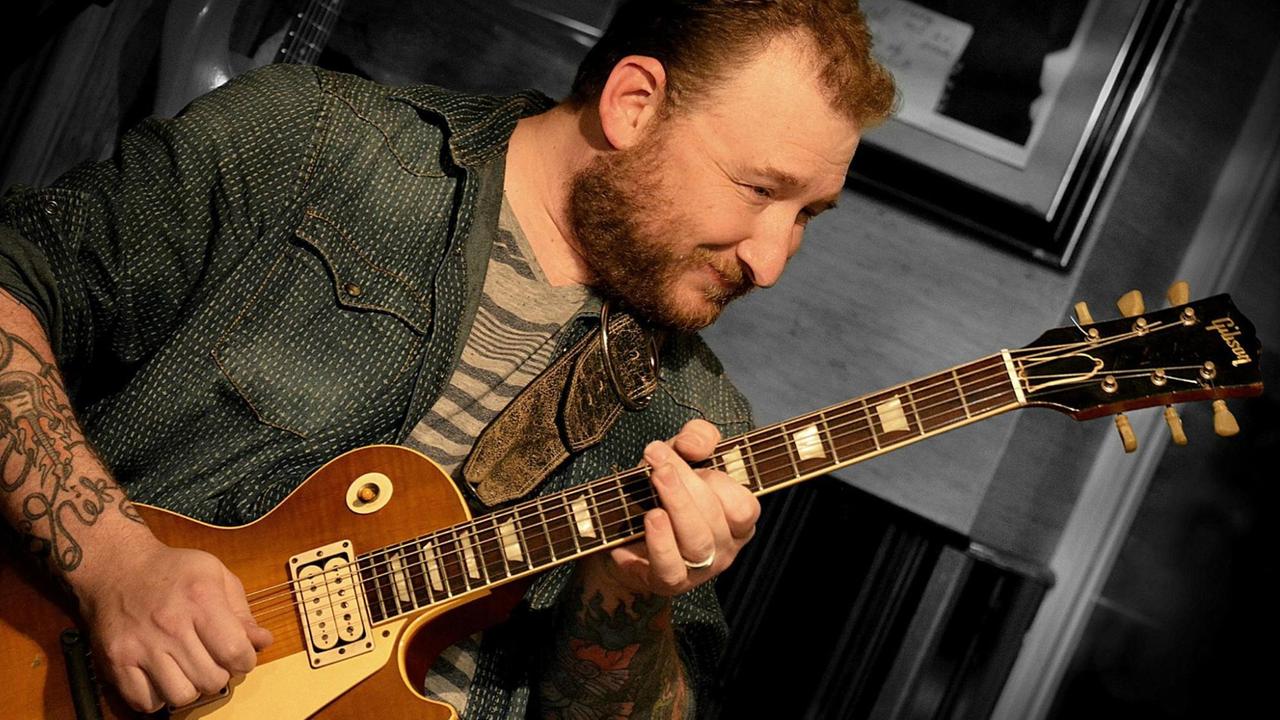 Ein bärtiger Mann beugt sich über seine Elektrogitarre und spielt. Ein bärtiger Mann beugt sich über seine Elektrogitarre und spielt.