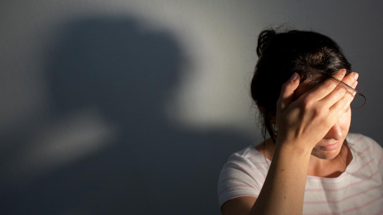 Eine Frau fasst sich an den Kopf, hinter ihr ist an der Wand ihr Schatten zu sehen. (Symbolfoto) Eine Frau fasst sich an den Kopf, hinter ihr ist an der Wand ihr Schatten zu sehen. (Symbolfoto)