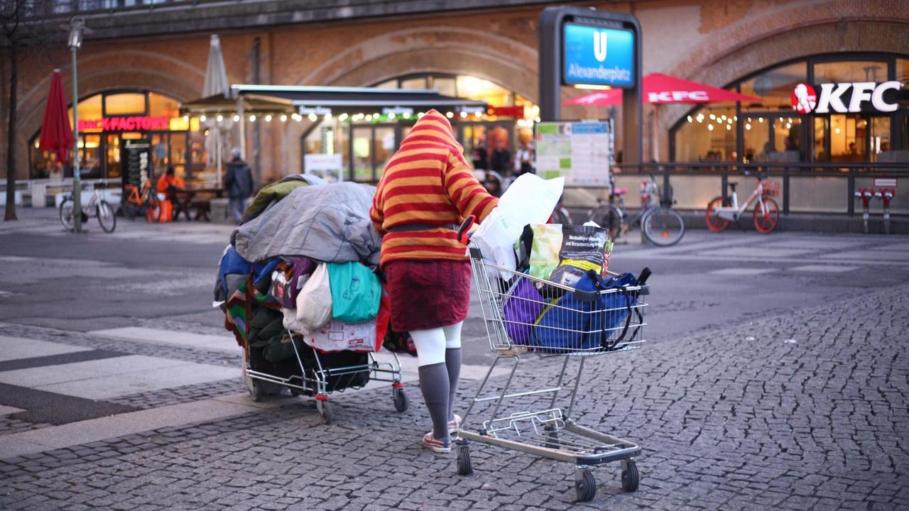 Eine Obdachlose Frau schiebt im Bezirk Mitte auf dem Alexanderplatz bei einbrechender Dämmerung ihre Habe in zwei Einkaufswagen über den Platz. 