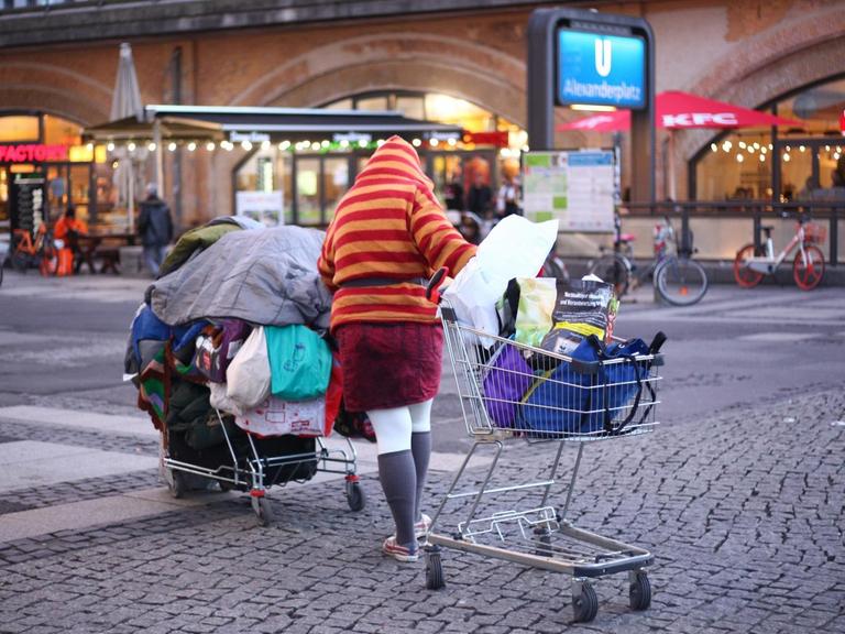 Eine Obdachlose Frau schiebt im Bezirk Mitte auf dem Alexanderplatz bei einbrechender Dämmerung ihre Habe in zwei Einkaufswagen über den Platz.