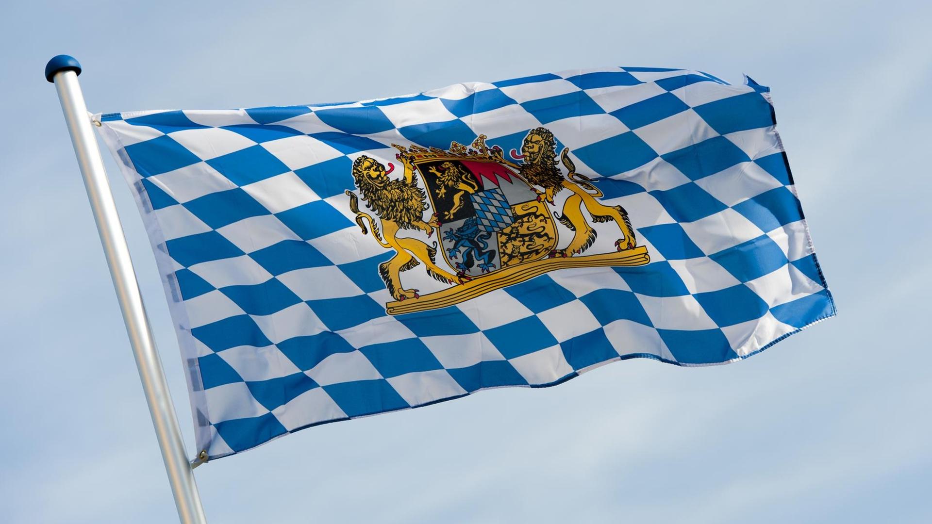 Ein blau-weiße Bayernfahne mit dem Wappen des Freistaats Bayern weht im Wind.
