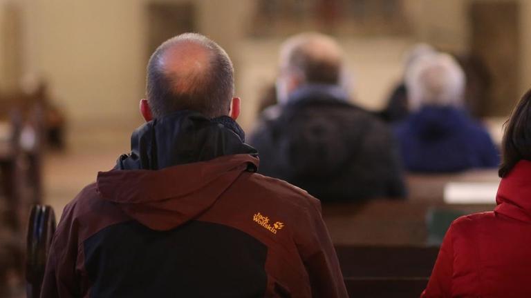 Besucher sitzen aufgrund der Corona-Pandemie mit Abstand zueinander in einer Kirche