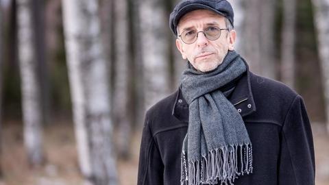 Erkki Sven Tüür trägt eine Mütze und Schal und steht vor einem Birkenwald.