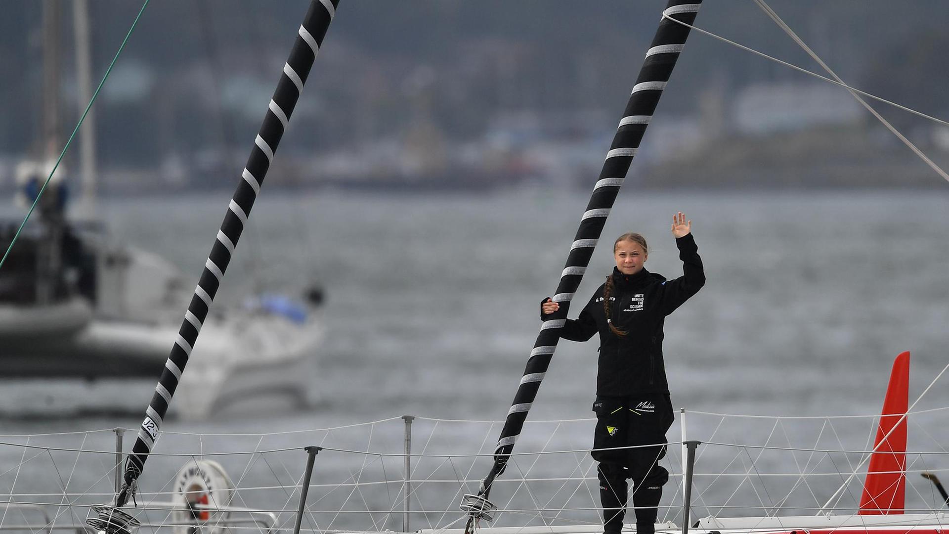 Greta Thunberg steht auf dem Deck des Segelbootes und winkt Richtung Kamera. Greta Thunberg steht auf dem Deck des Segelbootes und winkt Richtung Kamera.