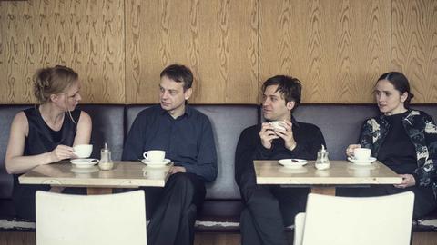 Die vier Musiker sitzen nebeneinander in einem Kaffe und sind in ein Gespräch vertieft