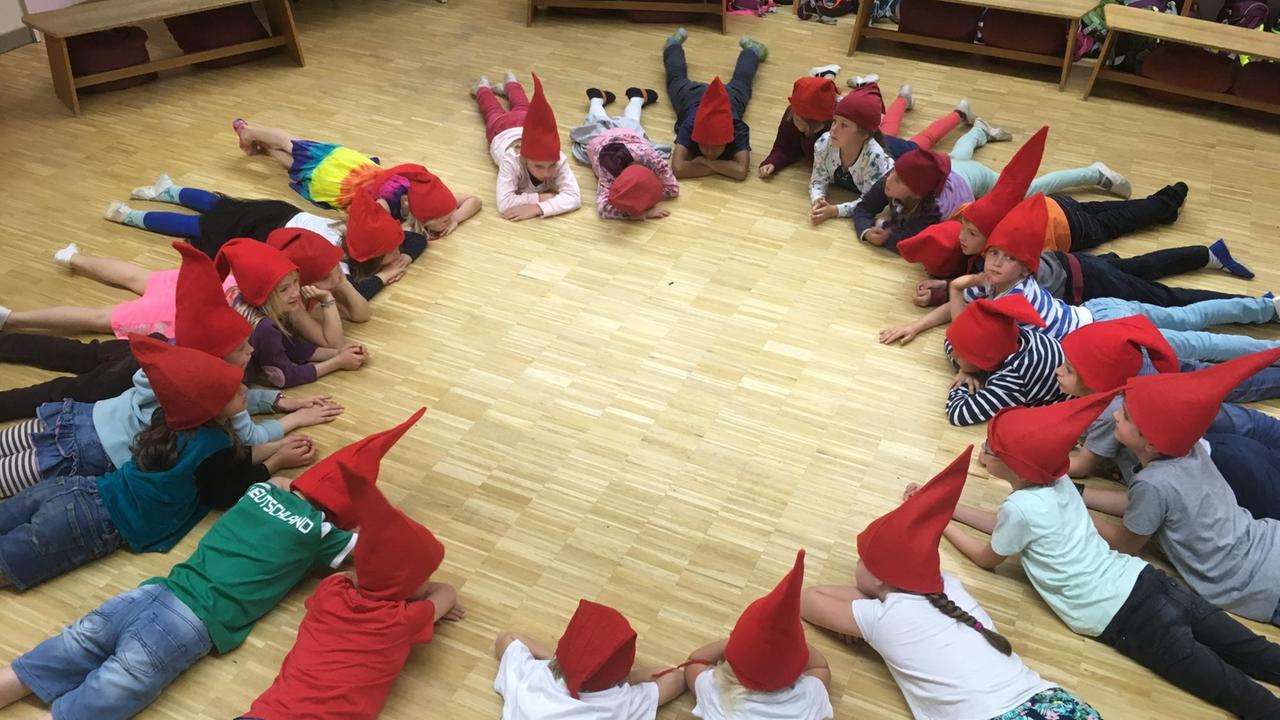 In einer Kölner Waldorfschule liegen die Kinder im Kreis - sie tragen rote Zipfelmützen In einer Kölner Waldorfschule liegen die Kinder im Kreis - sie tragen rote Zipfelmützen