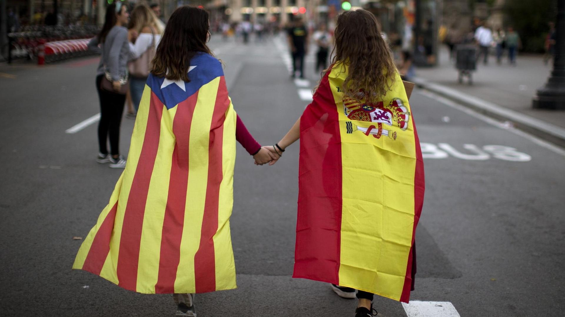Zwei junge Frauen, in die spanische Nationalflagge (r) sowie die katalanische Flagge "Estelada" gehüllt, halten sich am in Barcelona an der Hand. Zwei junge Frauen, in die spanische Nationalflagge (r) sowie die katalanische Flagge "Estelada" gehüllt, halten sich am in Barcelona an der Hand.