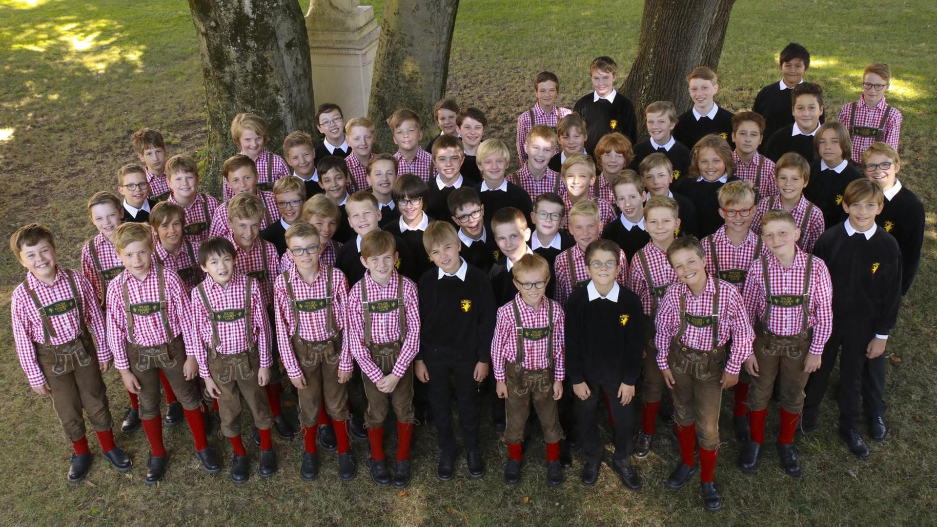 Das Foto zeigt den Tölzer Knabenchor aus der Vogelperspektive. Die Jungen tragen Lederhosen und karierte Hemden und schauen lächelnd nach oben in die Kamera. Das Foto zeigt den Tölzer Knabenchor aus der Vogelperspektive. Die Jungen tragen Lederhosen und karierte Hemden und schauen lächelnd nach oben in die Kamera.