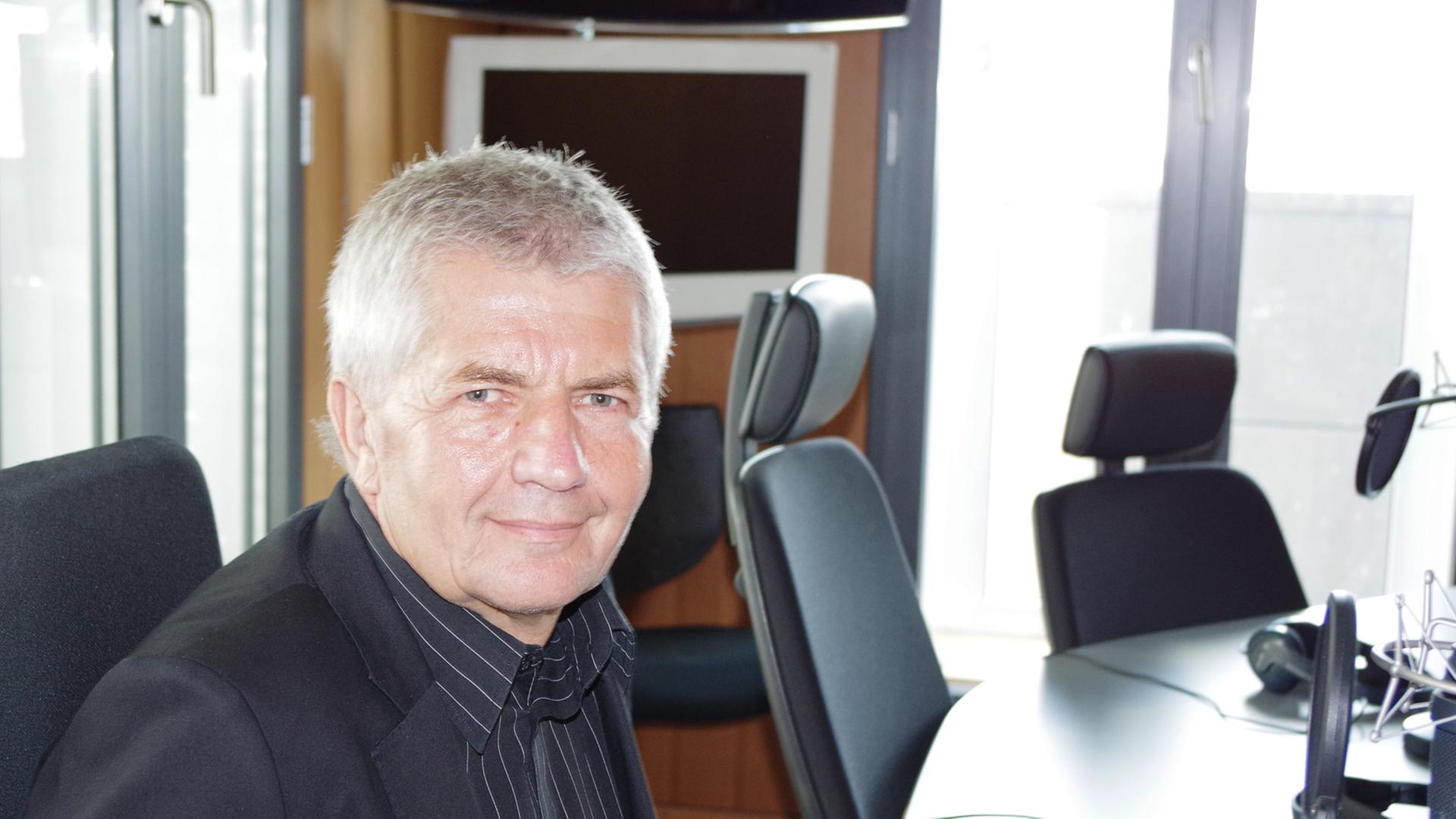 Roland Jahn sitzt an einem Tisch vor einem Mikrofon in einem Studio des Hauptstadtbüro des Deutschlandfunks und lächelt in die Kamera.