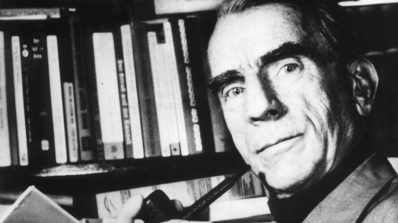 Ein schwarzweißes, undatiertes Foto zeigt den deutschen Schriftsteller, Widerstandskämpfer und Mitherausgeber des "Ulenspiegel", Günther Weisenborn mit Tabakpfeife und geöffnetem Buch in der Hand vor Buchregal Ein schwarzweißes, undatiertes Foto zeigt den deutschen Schriftsteller, Widerstandskämpfer und Mitherausgeber des "Ulenspiegel", Günther Weisenborn mit Tabakpfeife und geöffnetem Buch in der Hand vor Buchregal