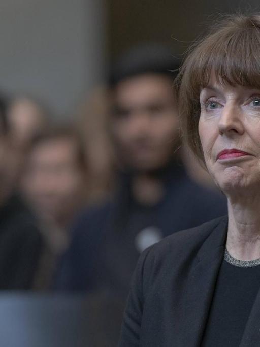 Henriette Reker sitzt in einem Saal und hört einer Rede zu.