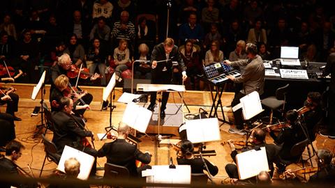 Mark Romboy und die Dortmunder Philharmoniker präsentieren ihre Version von Debussy. Man sieht Streicher und Dirigent vor Publikum sowie Mark Romboy am Synthesizer.