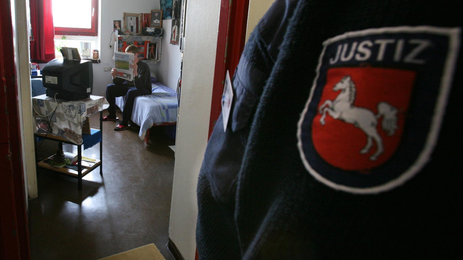 Ein 19-jähriger Häftling sitzt in seiner Zelle im Jugendgefängnis Hameln, im Vordergrund ist das niedersächsische Justizabzeichen auf dem Ärmel eines Justizbeamten zu sehen.
