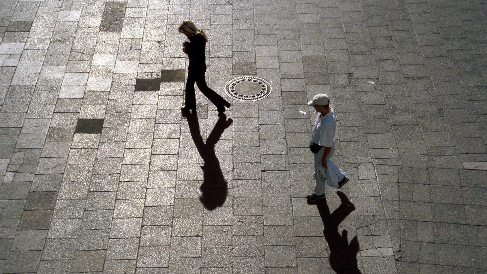 Mann verfolgt Frau, beide werfen Schatten auf den Steinboden Mann verfolgt Frau, beide werfen Schatten auf den Steinboden
