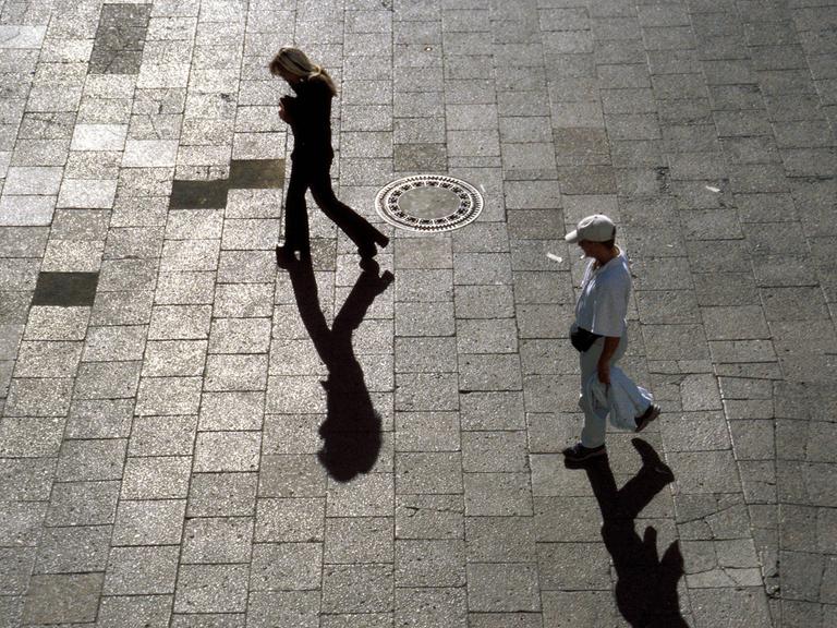 Mann verfolgt Frau, beide werfen Schatten auf den Steinboden