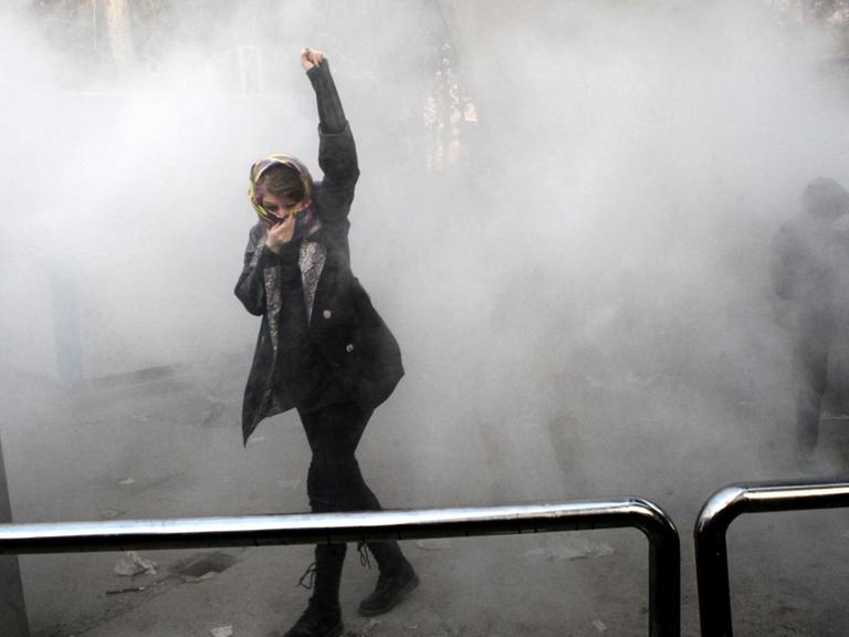 An Iranian woman raises her fist amid the smoke of tear gas at the University of Tehran during a protest driven by anger over economic problems, in the capital Tehran on December 30, 2017. Students protested in a third day of demonstrations sparked by anger over Iran's economic problems, videos on social media showed, but were outnumbered by counter-demonstrators. / AFP PHOTO / STR