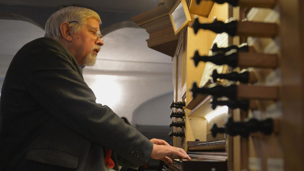 Musikprofessor Harald Vogel spielt auf der Ahrend-Orgel in der Zionskirche in Worpswede in Niedersachsen, wobei die gedrechselten Registerzüge im Vordergrund teilweise gezogen sind.