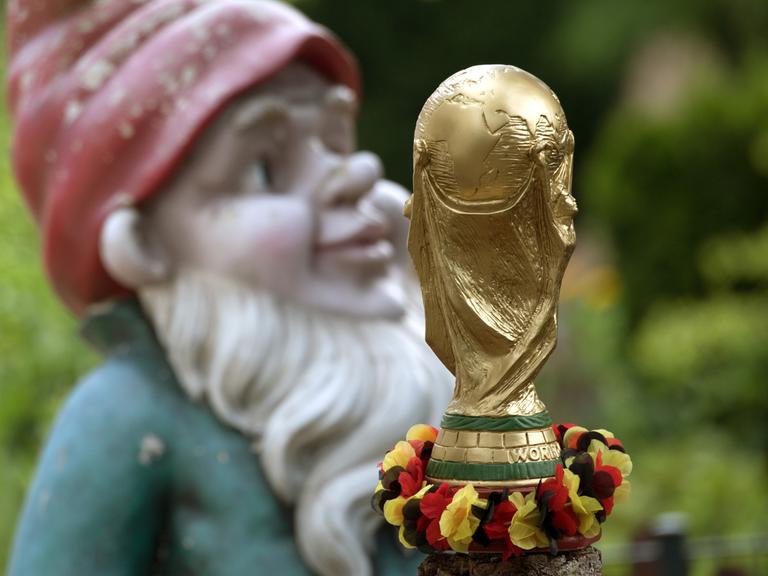 Ein nachgebildeter FiFA-WM-Pokal mit einer Girlande in den deutschen Nationalfarben und ein großer Gartenzwerg stehen in einem Vorgarten in Kleinmachnow (Brandenburg).
