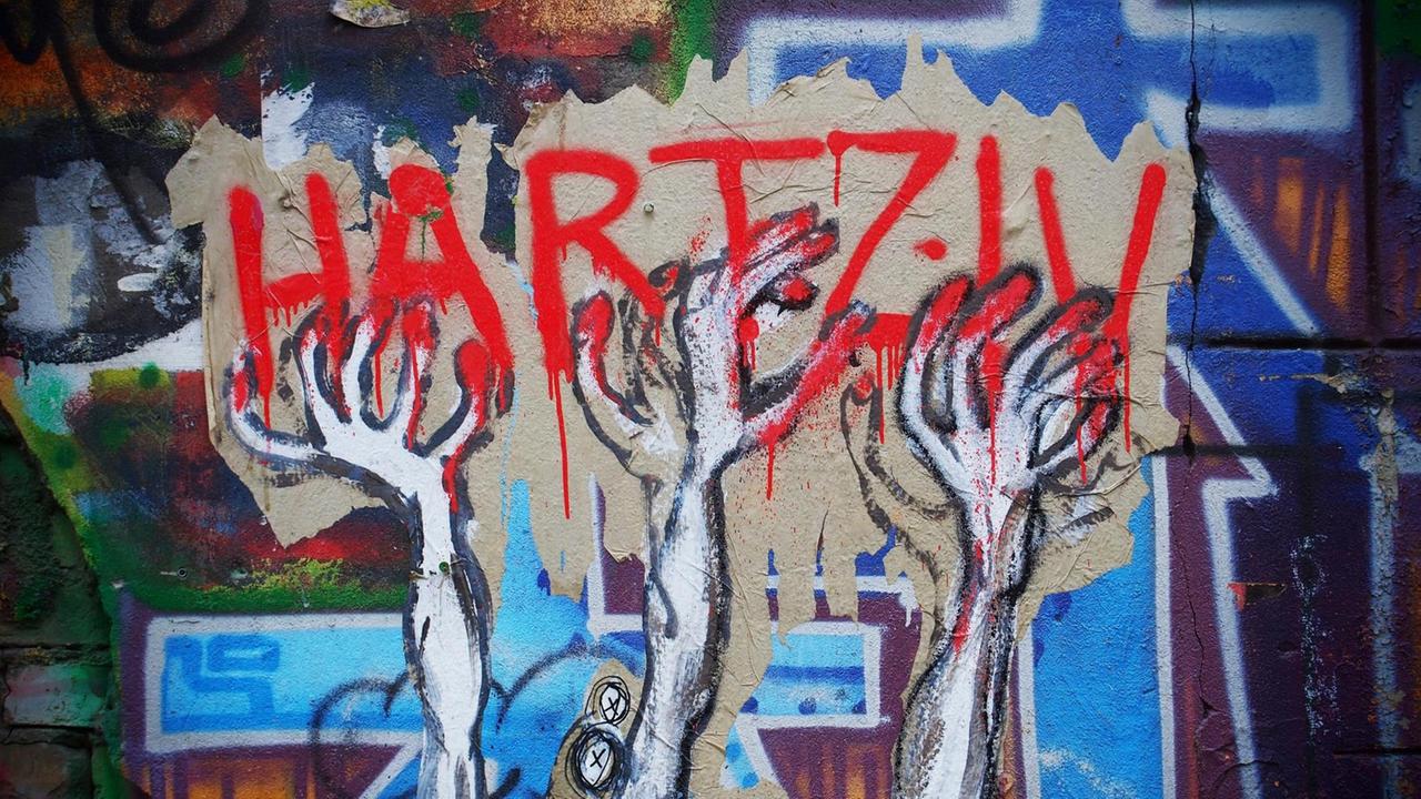 Ein unbekannter Street-Art-Künstler hat auf einer Mauer an einem besetzten Haus in Berlin im Bezirk Mitte dieses Bild geschaffen, das seine Meinung zu den Hartz IV Gesetzen drastisch wiedergibt: Verzwifelte HÄnde greifen nach dem roten Schriftzug Hartz IV, im Hintergrund sind Grabkreuze zu sehen. Ein unbekannter Street-Art-Künstler hat auf einer Mauer an einem besetzten Haus in Berlin im Bezirk Mitte dieses Bild geschaffen, das seine Meinung zu den Hartz IV Gesetzen drastisch wiedergibt: Verzwifelte HÄnde greifen nach dem roten Schriftzug Hartz IV, im Hintergrund sind Grabkreuze zu sehen.