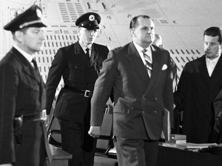 Der Angeklagte Oswald Kaduk wird von drei Polizisten in einen Gerichtssaal geführt.