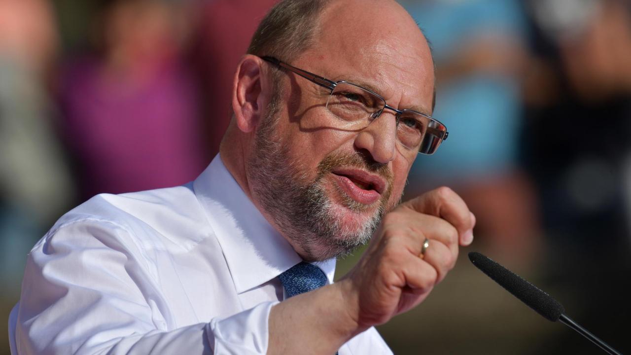 Schulz spricht mit erhobener rechter Hand in ein Mikrofon.