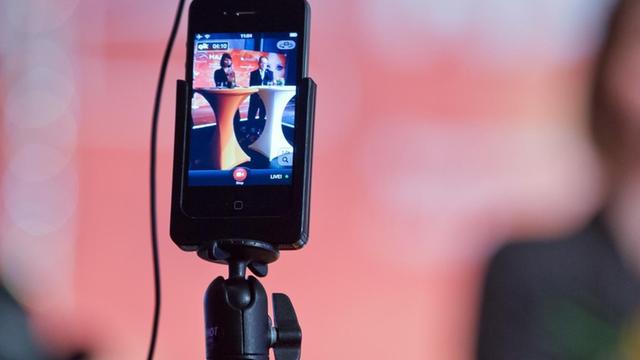 Ein Smartphone ist während einer Pressekonferenz auf einem Stativ angebracht, um diese zu filmen.
